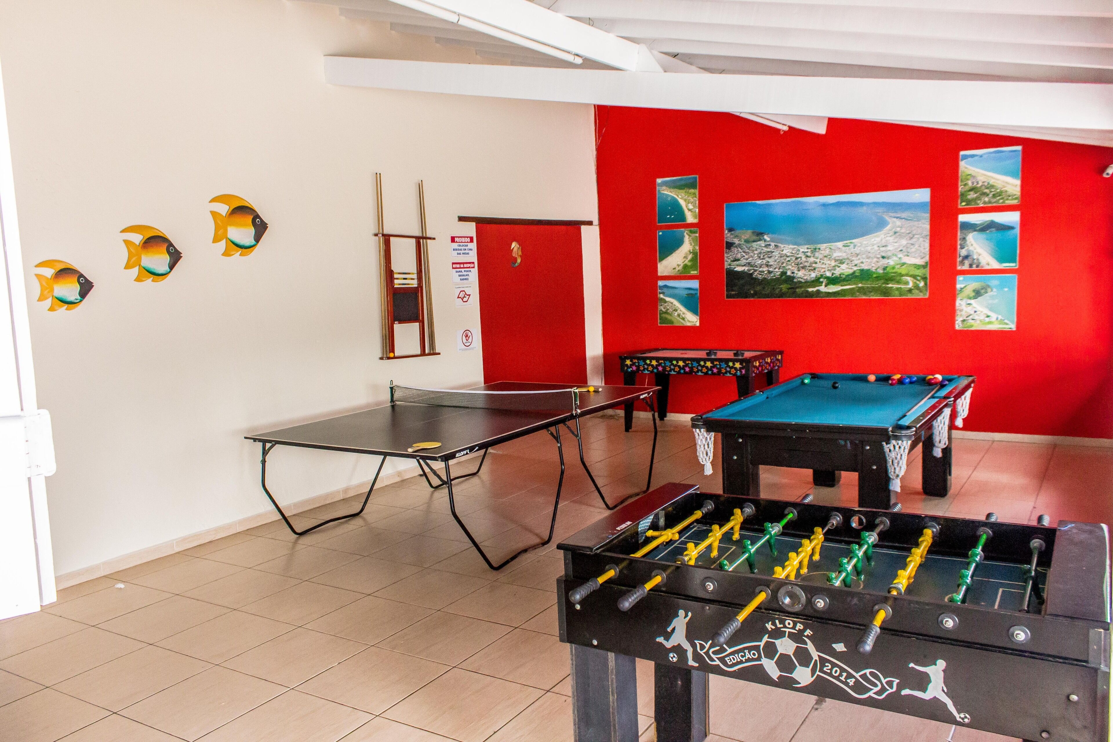 Quarto com mesa de pebolim, mesa de tênis de mesa e mesa de bilhar.