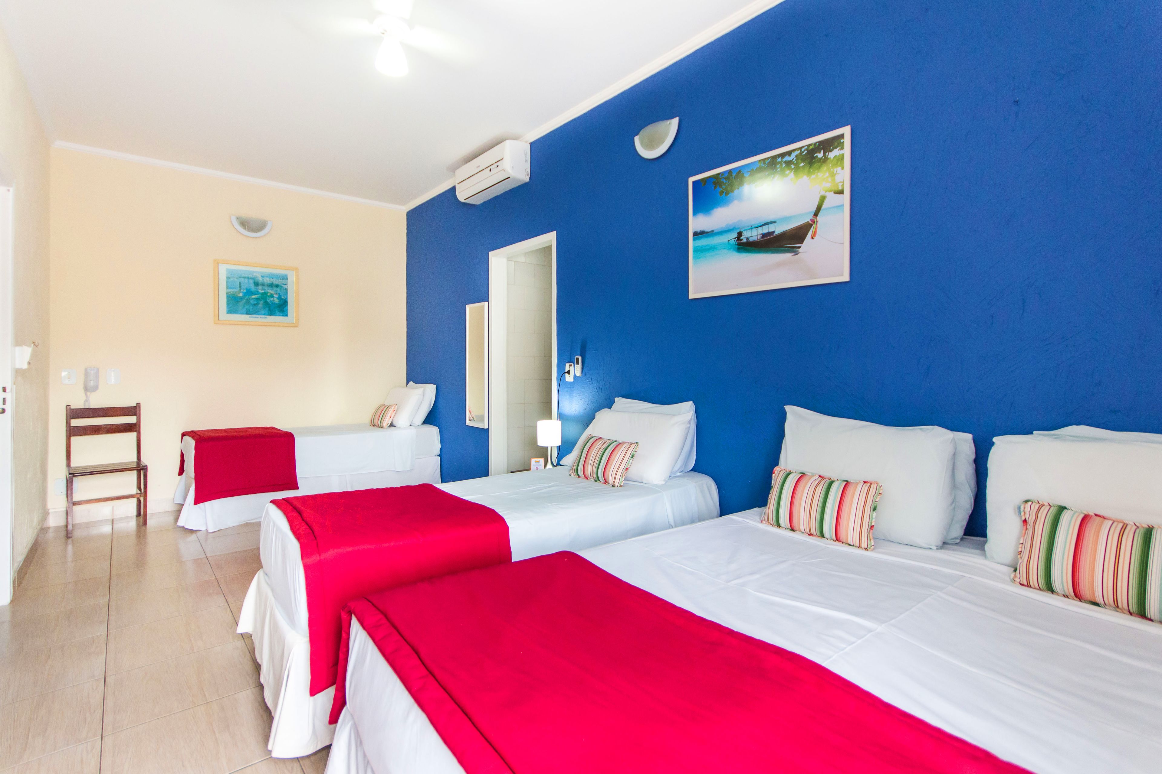 A hotel room with two beds, a red and white color scheme, a painting of a boat on the wall, and a wooden chair.