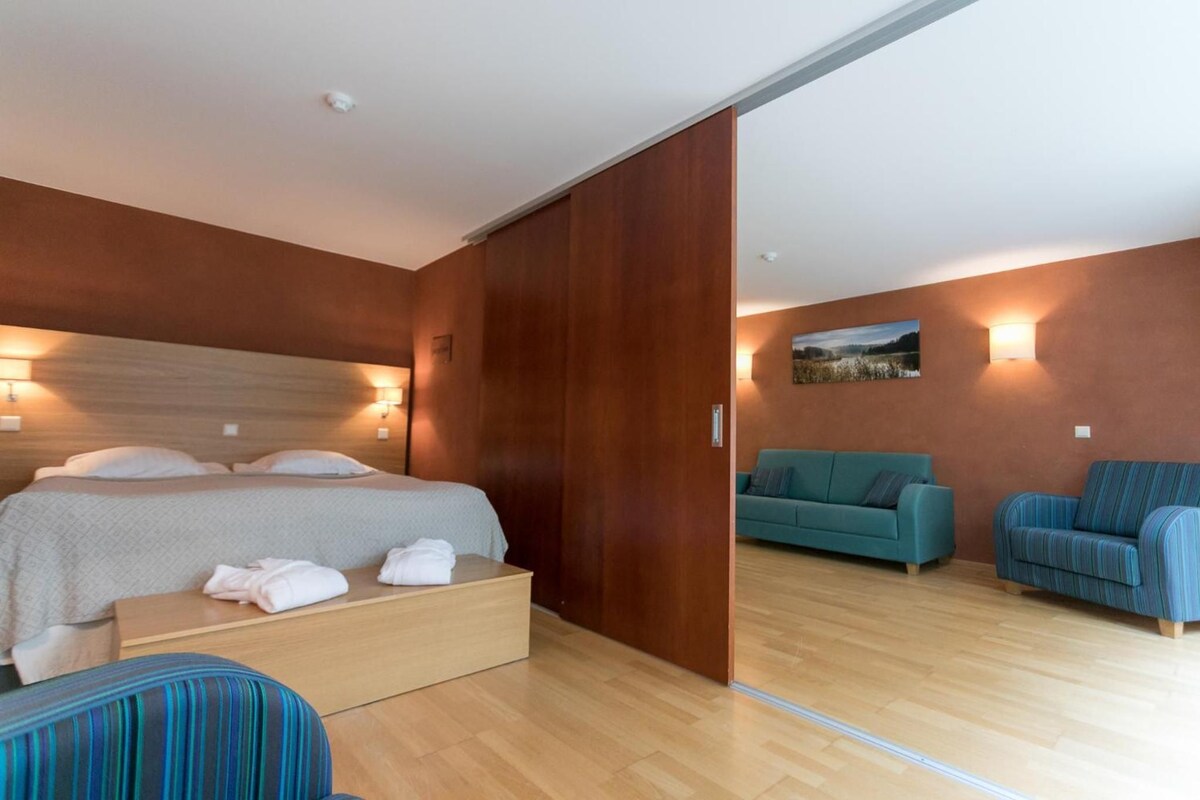 Una habitación de hotel con una cama, una mesita de noche de madera, un sofá azul y un sillón azul.