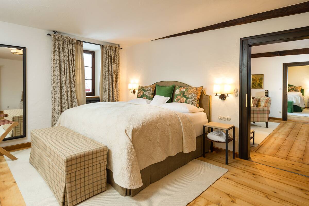 A bedroom with a large bed, bedside tables, a bench, and a mirror.