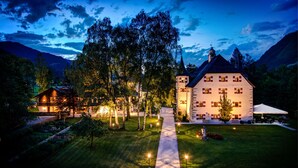 A large, well-lit building with a tower, surrounded by trees and a pathway leading to it. - Schloss Prielau Hotel & Restaurants (Zell am See)
