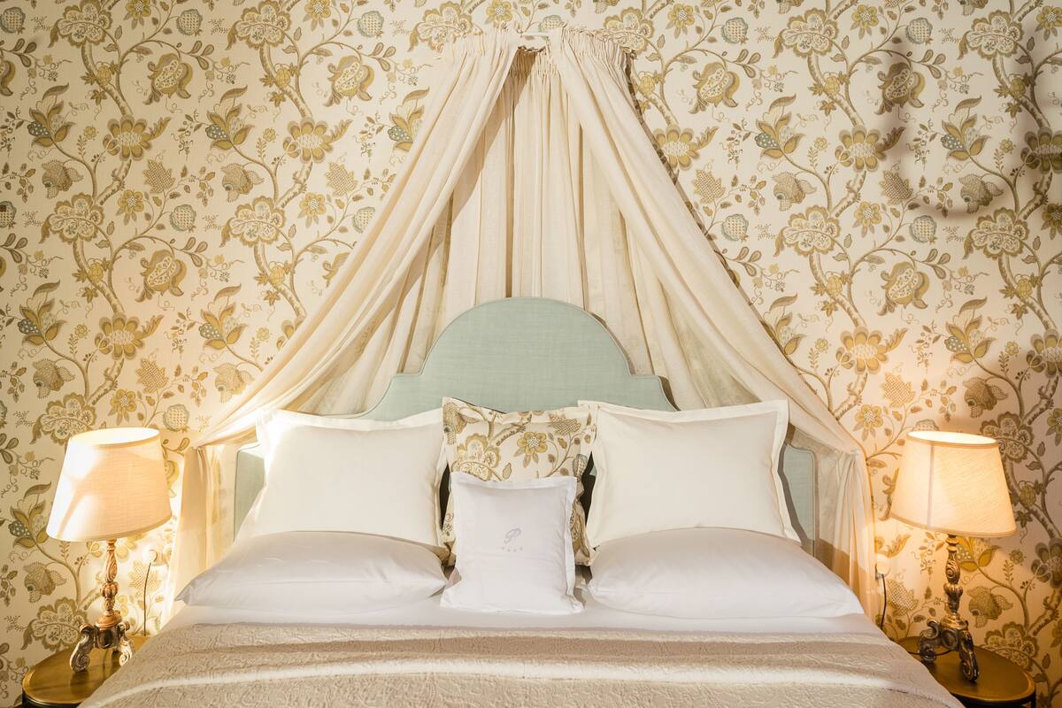 A bed with a canopy, floral wallpaper, and two bedside lamps.