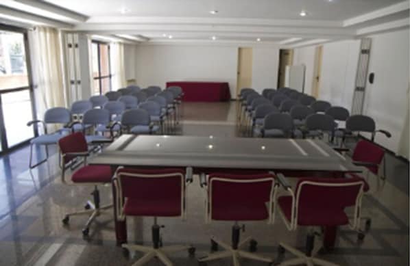A conference room with a large rectangular table surrounded by rows of chairs, large windows, and a red carpet. - Spazzio Hotel Residence (Fortaleza)
