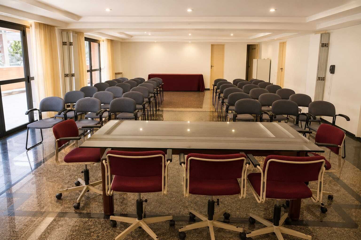 A conference room with a large table and rows of chairs, carpeted floor, and large windows.