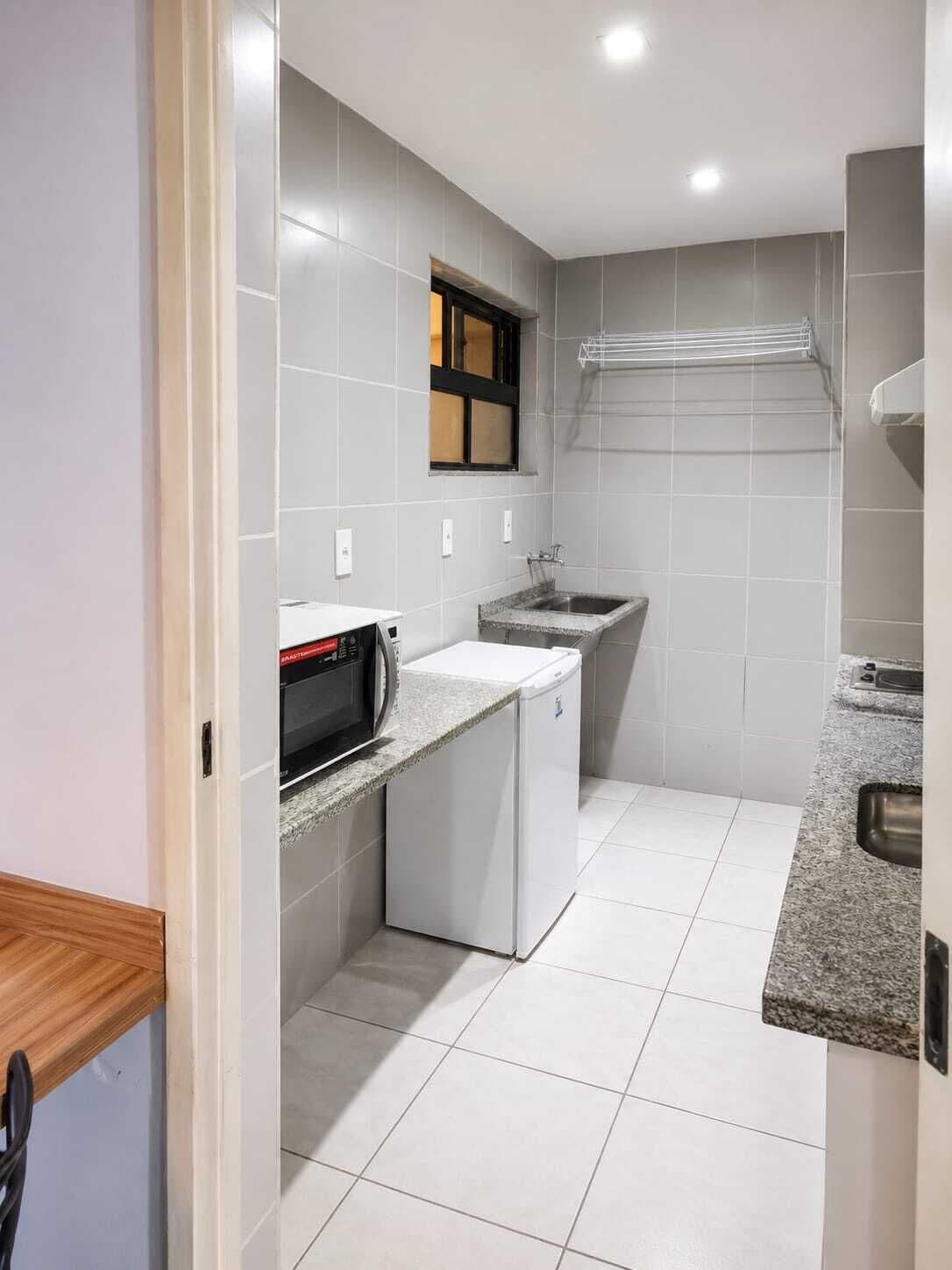 A compact kitchen with a microwave, a small refrigerator, a sink, and a window.