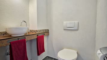 A bathroom with a white sink, a red towel, a white toilet, and a wall-mounted light fixture.