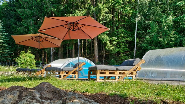 Un terrain de camping équipé d’une tente, de chaises longues et de deux grands parasols.