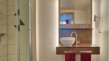 Ein Badezimmer mit einer Duschkabine aus Glas, einem weißen Waschbecken mit Holzbeschlag und einem Spiegel darüber.