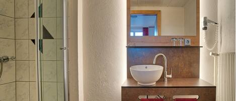 A bathroom with a glass shower enclosure, a white sink with a wooden countertop, and a mirror above the sink.