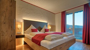 Une chambre moderne avec un cadre de lit en bois, une grande tête de lit et une vue sur l’extérieur grâce à une porte-fenêtre coulissante.