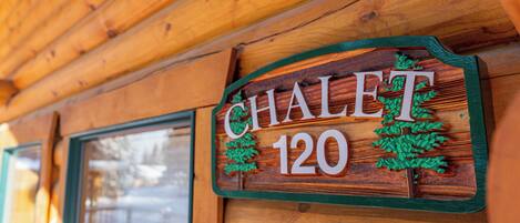 Een houten bord met de tekst 'CHALET 120' en twee illustraties van bomen.