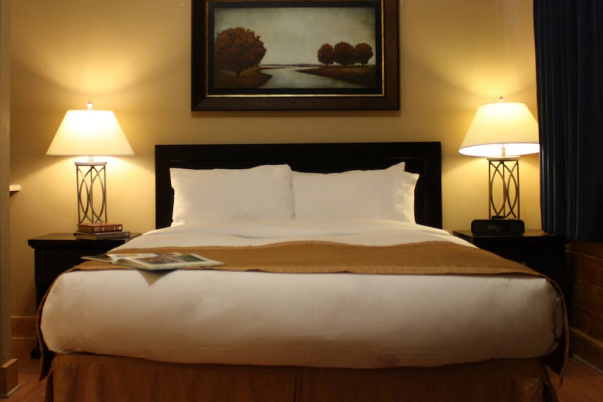 A hotel room with a large bed, two bedside lamps, a framed picture above the bed, and a wooden headboard.