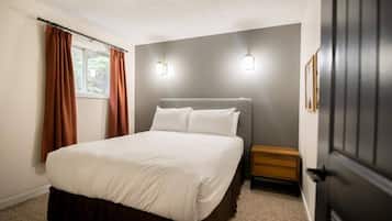 A bedroom with a bed, a nightstand, a window with curtains, and wall-mounted lighting.