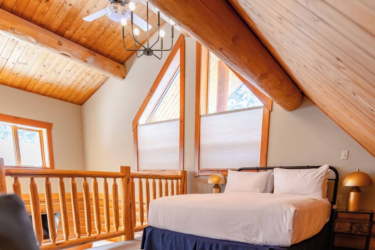 A bedroom with a bed, a chair, a wooden stool, a nightstand, and a ceiling fan.