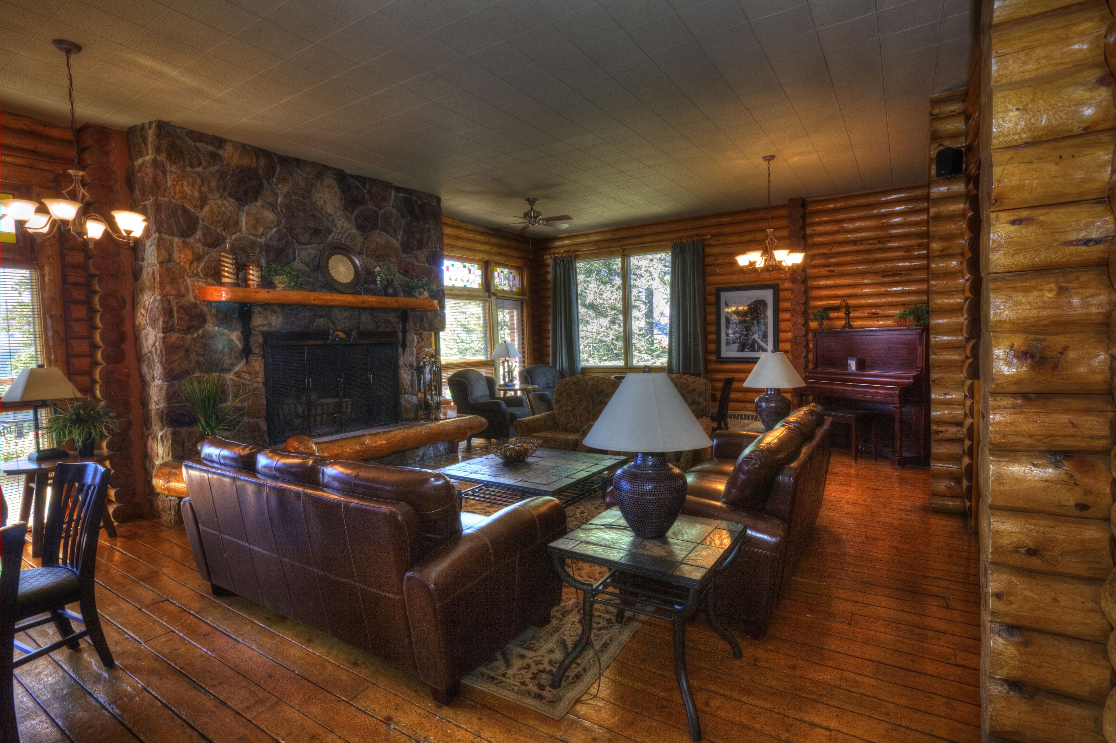 A log cabin interior with a stone fireplace, leather furniture, and wooden floors.