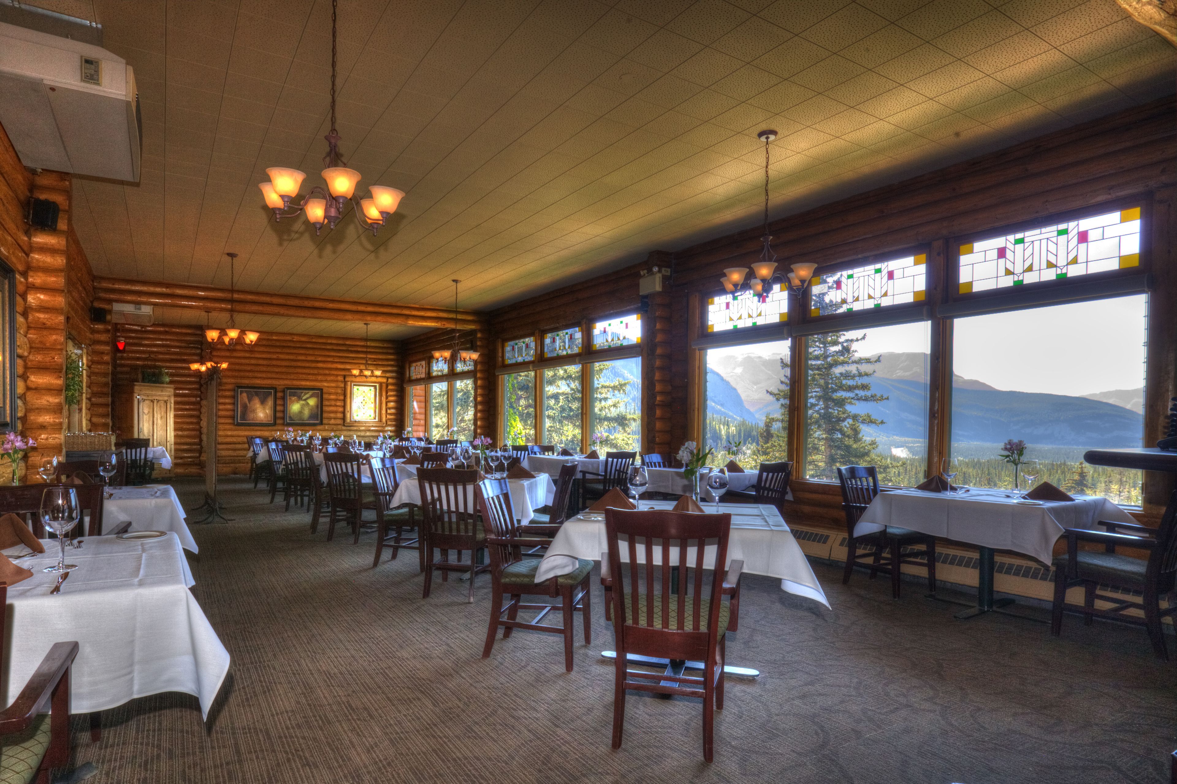 A restaurant with wooden walls, large windows, and tables set for dining.