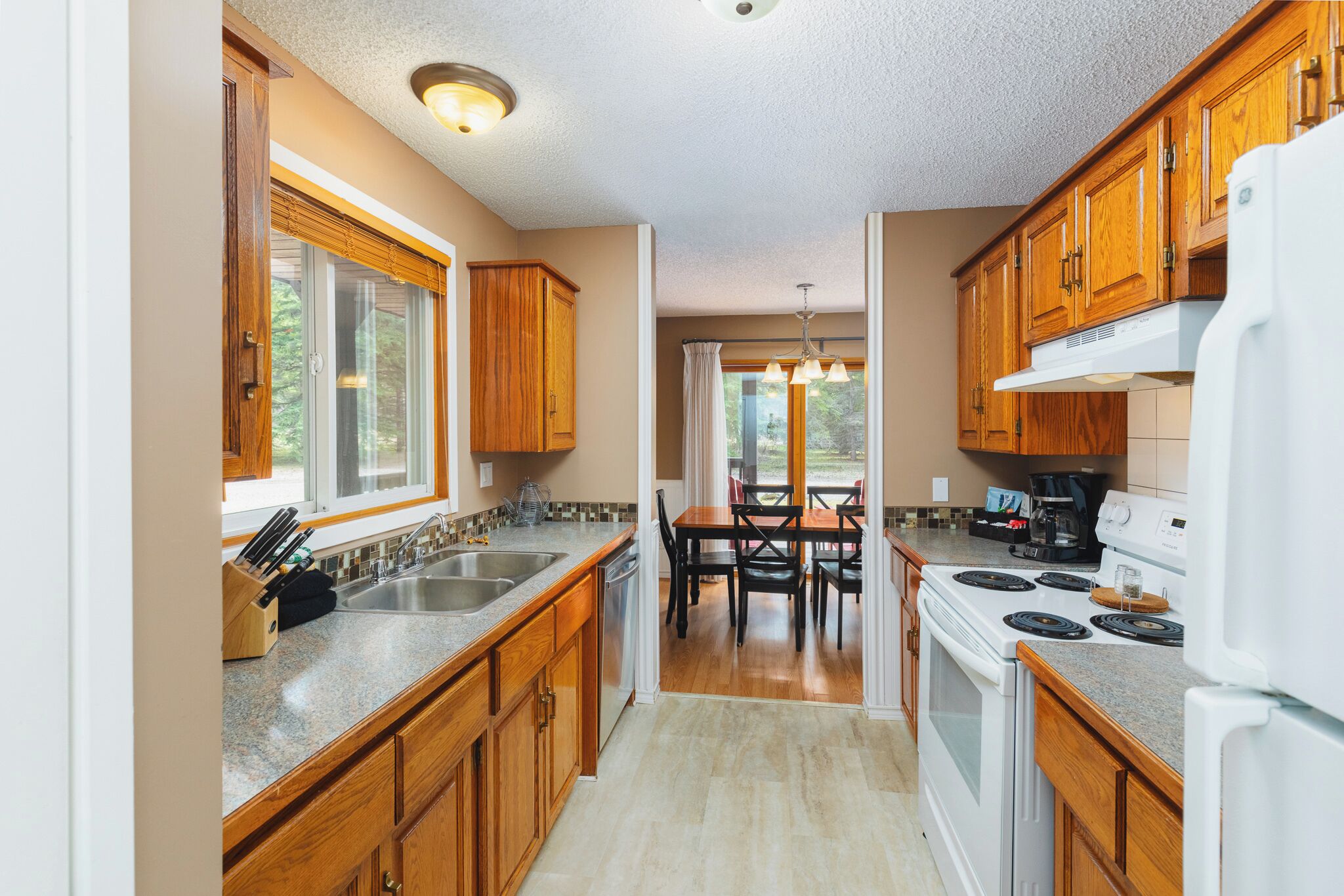 A kitchen with wooden cabinets, a granite countertop, a stove, and a dining area with a table and chairs.