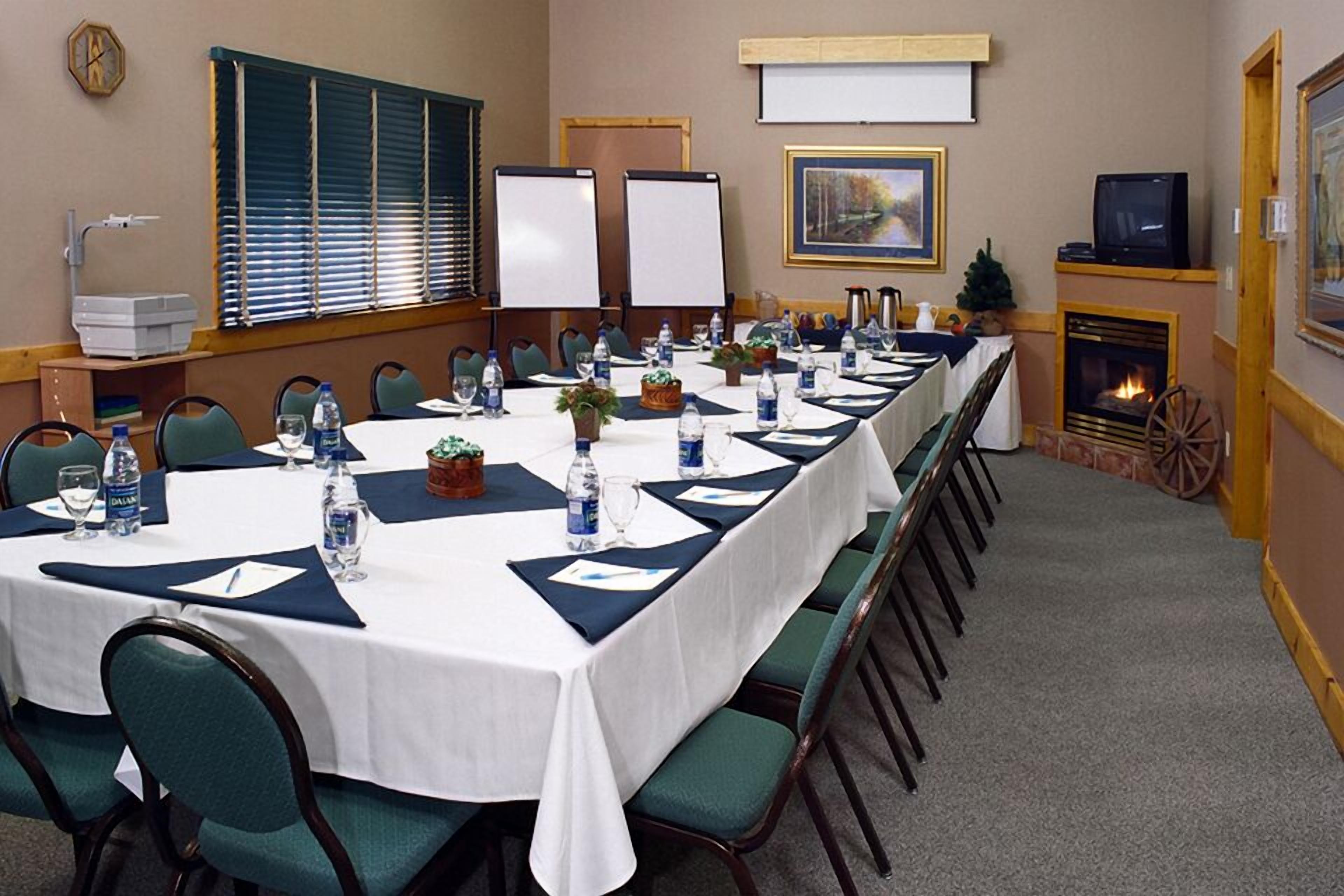 Une salle de conférence avec une longue table, des chaises, un projecteur, une cheminée et une horloge au mur.