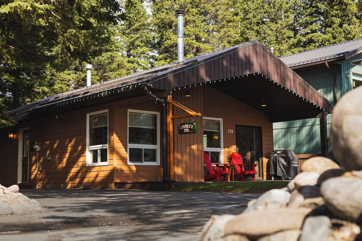 A wooden building with a covered porch, a sign reading "Chalet 126", and red chairs outside.