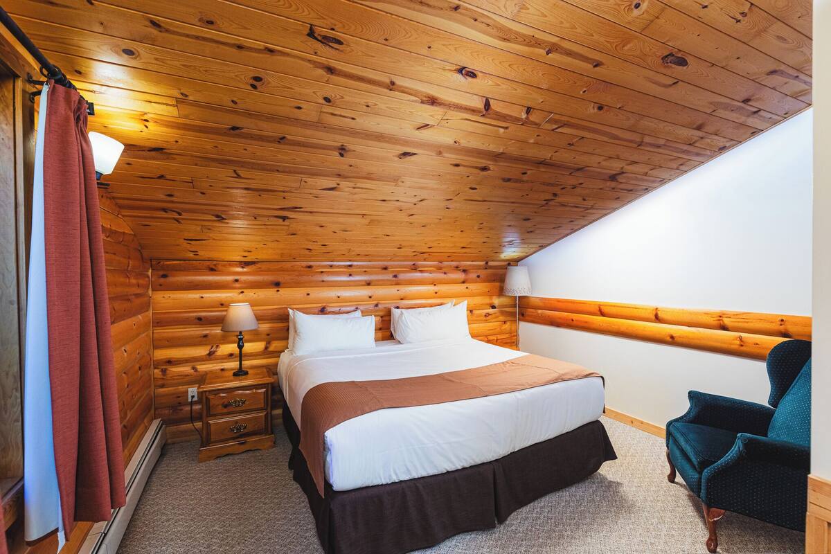 A wooden-paneled bedroom with a bed, bedside lamp, and a chair.