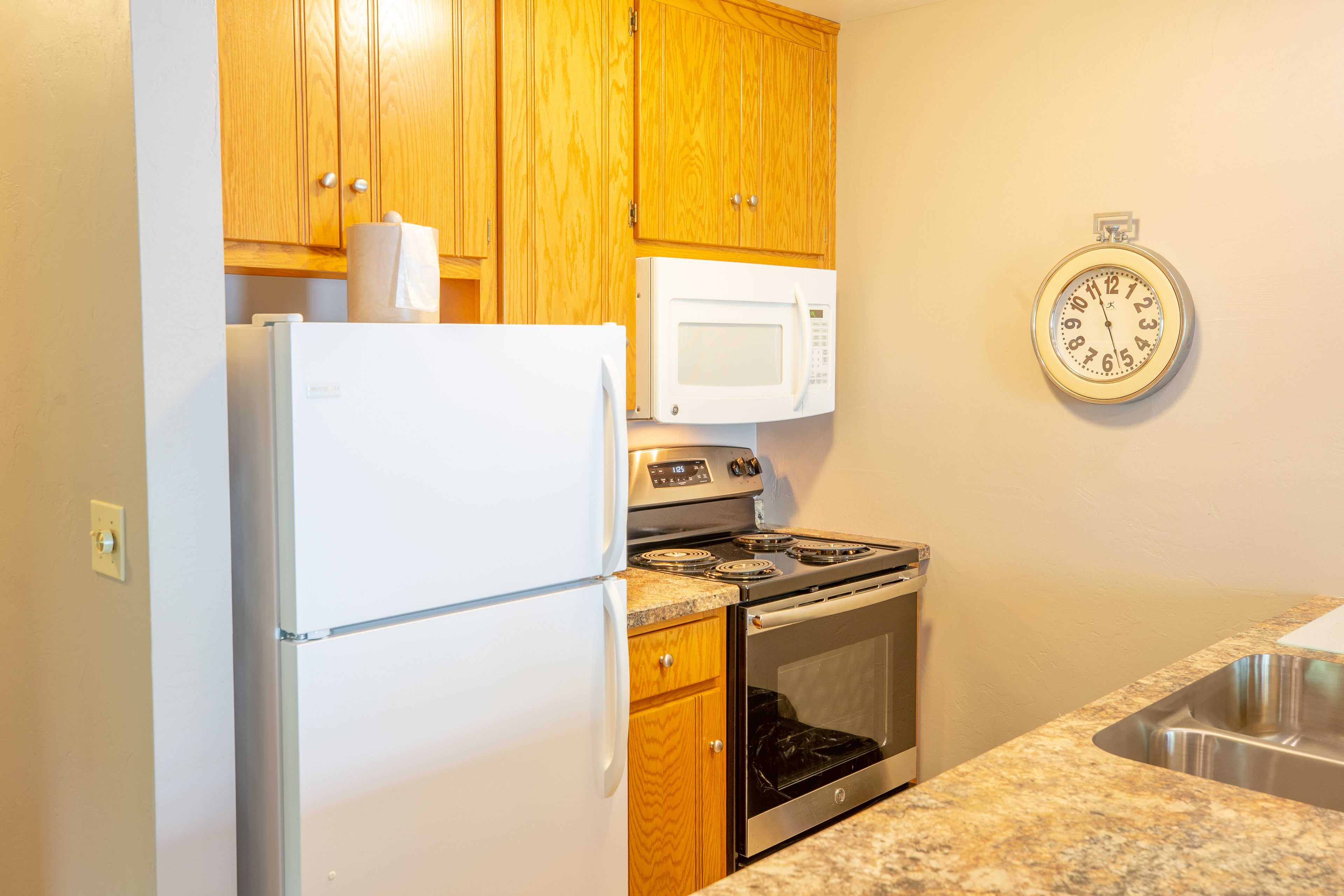 A kitchen with wooden cabinets, a white refrigerator, a microwave, an oven, and a sink.