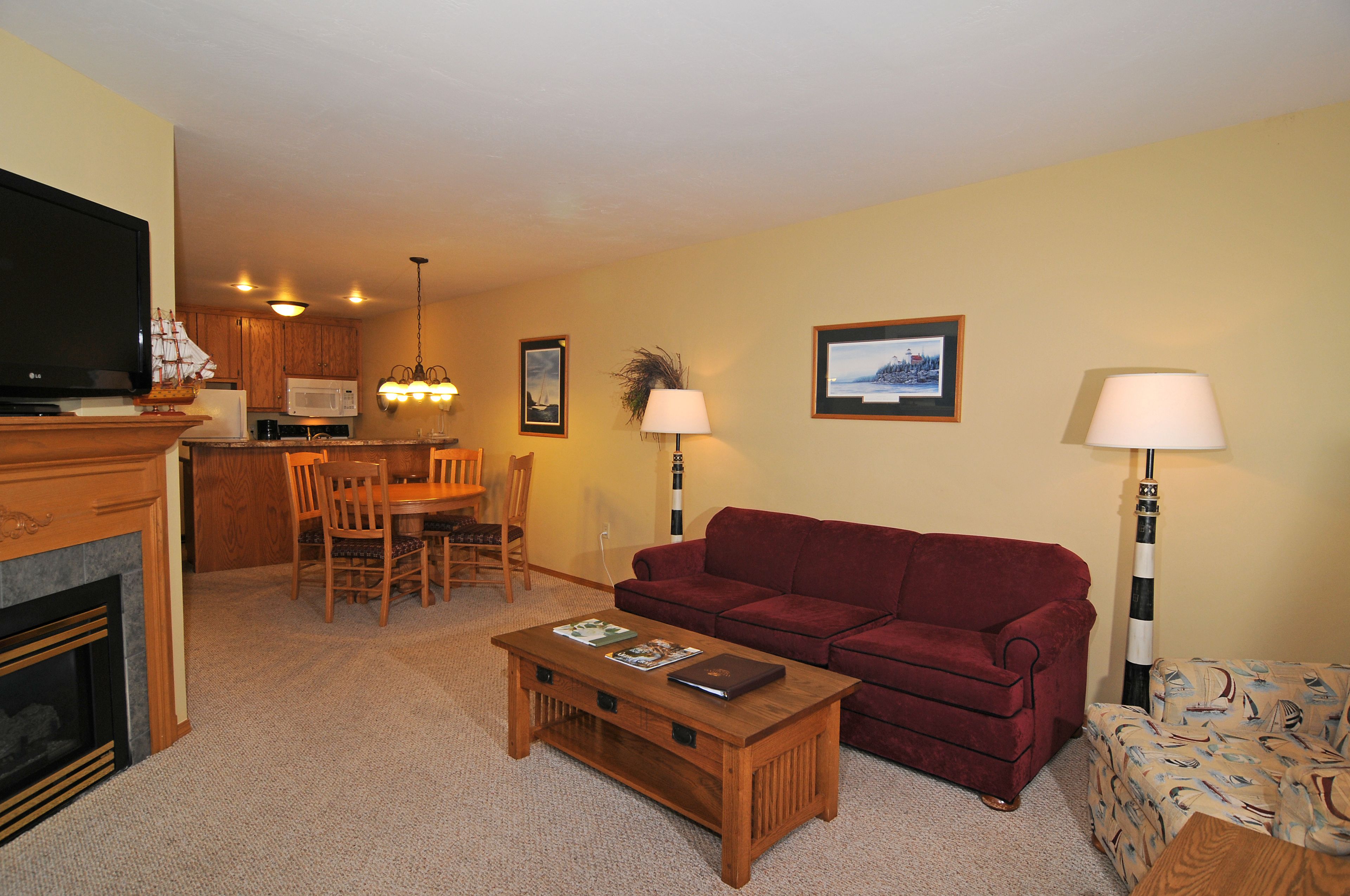 A living room with a red sofa, a wooden coffee table, a dining area with a wooden table and chairs, a fireplace, and a kitchen area with a microwave.