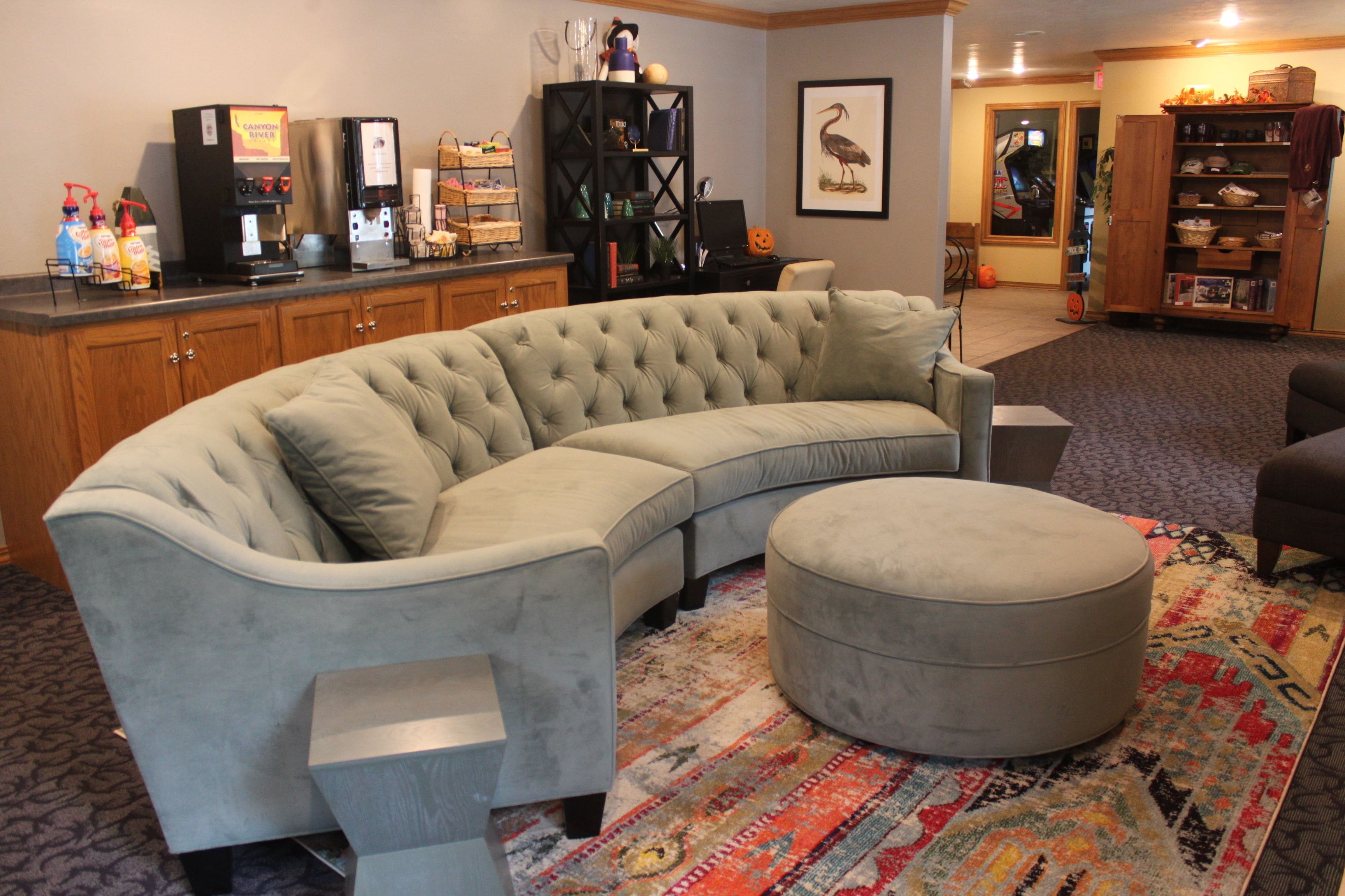 A living room with a sectional sofa, ottoman, and a coffee station.