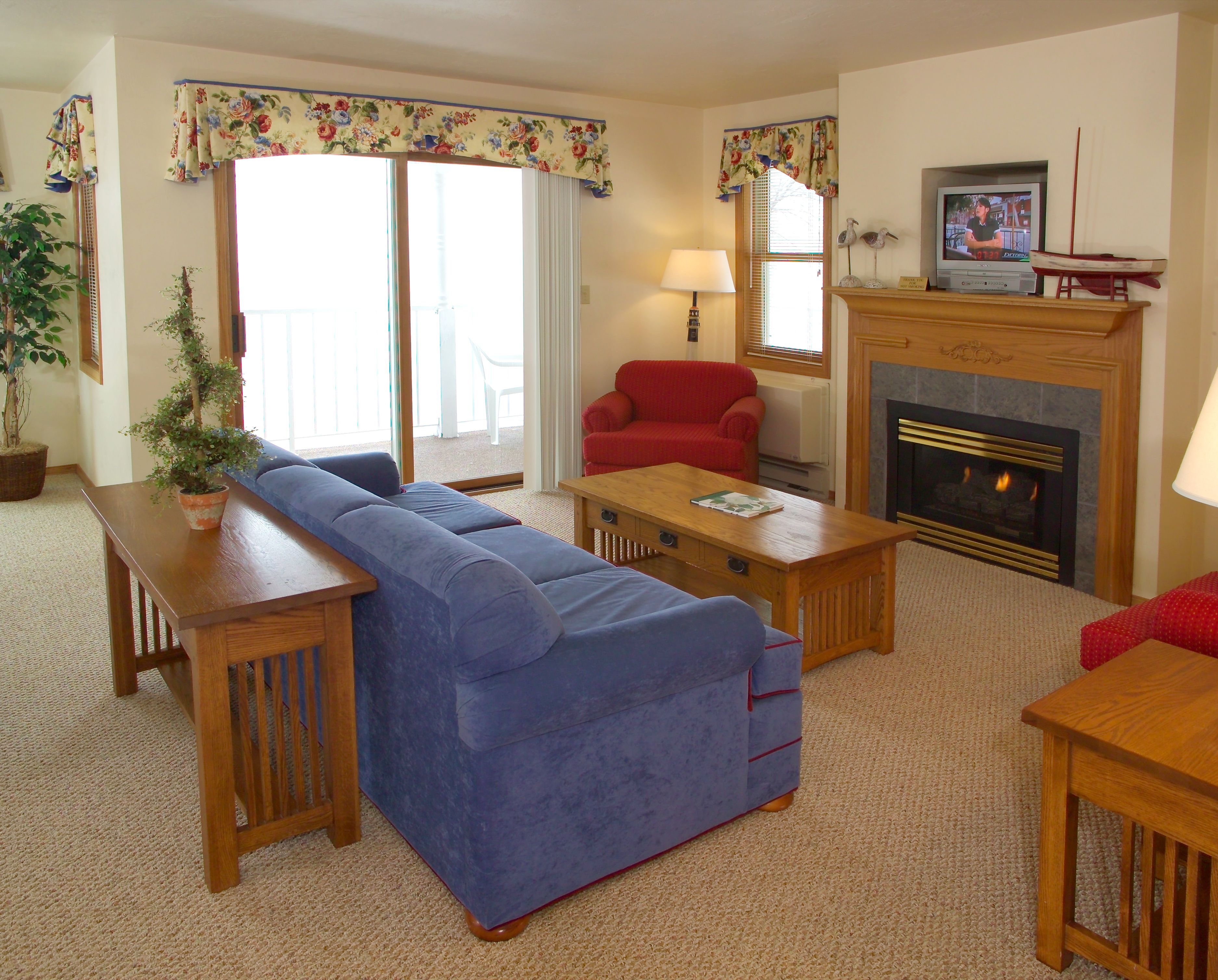 A living room with a blue sofa, a red armchair, a wooden coffee table, a fireplace, and a television on a mantel.