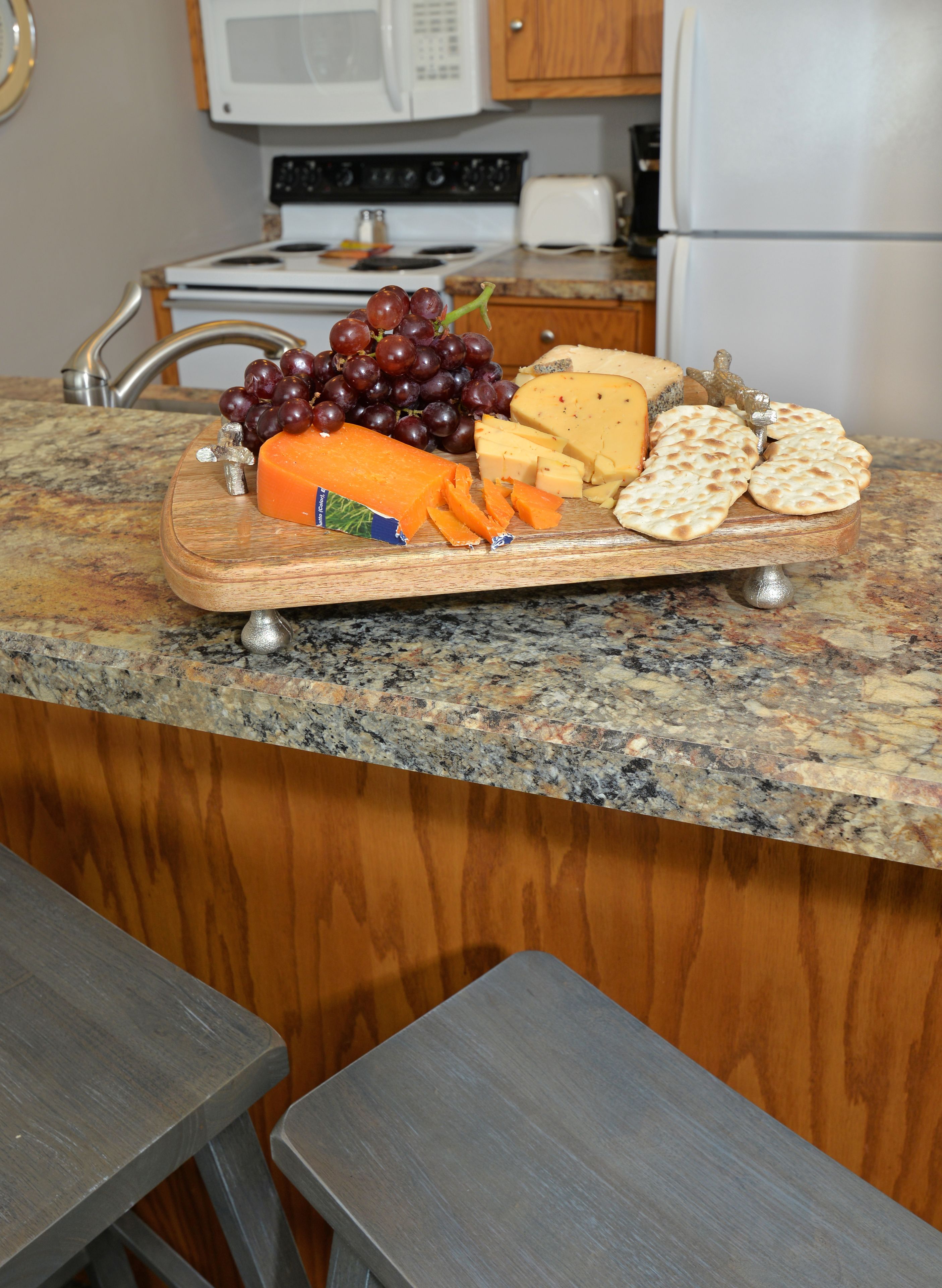 A kitchen counter with a cheese board featuring various cheeses, grapes, and flatbread.