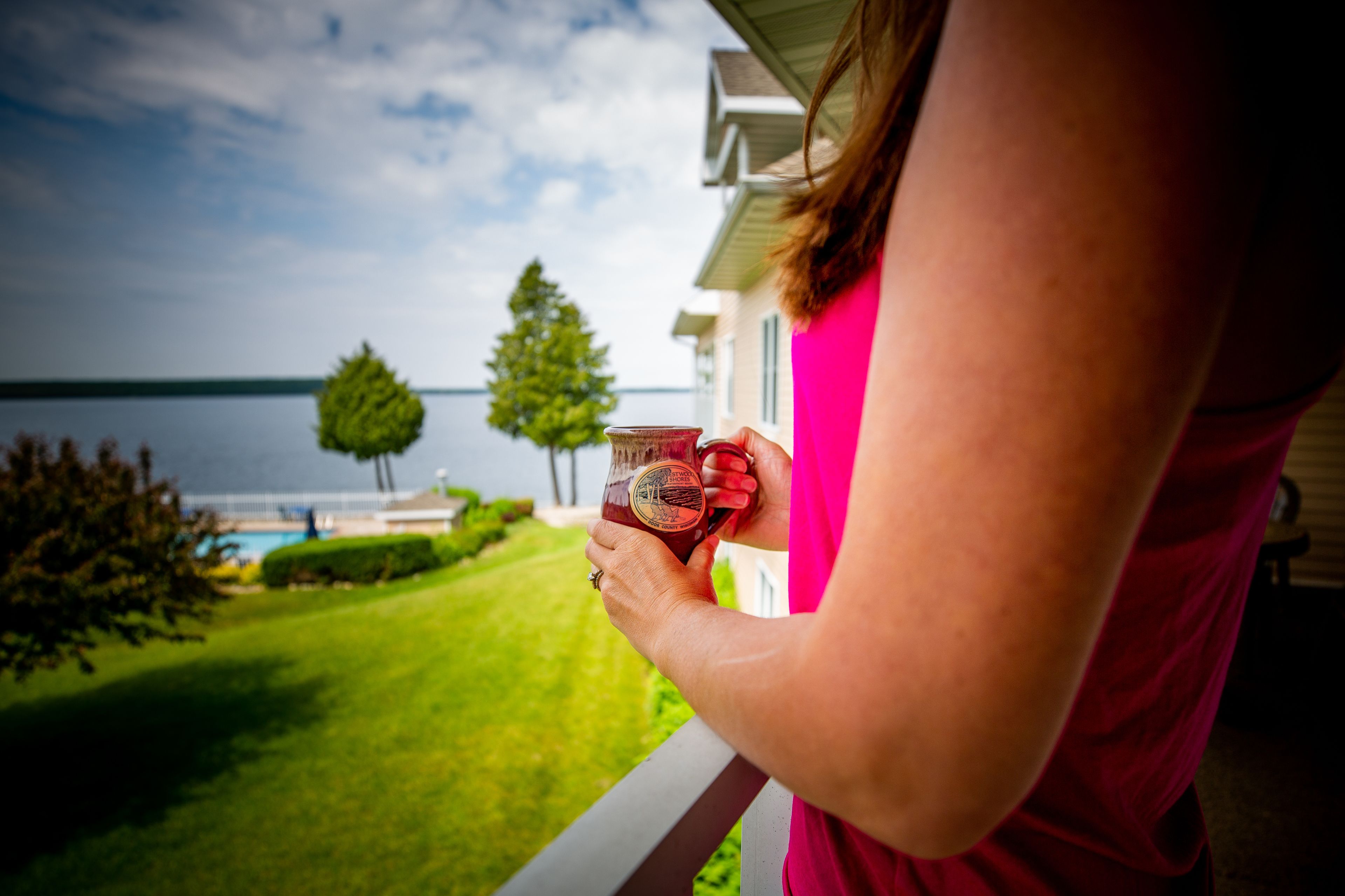 A person holding a mug on a balcony overlooking a lake.