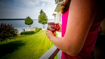 A person holding a mug on a balcony overlooking a lake.