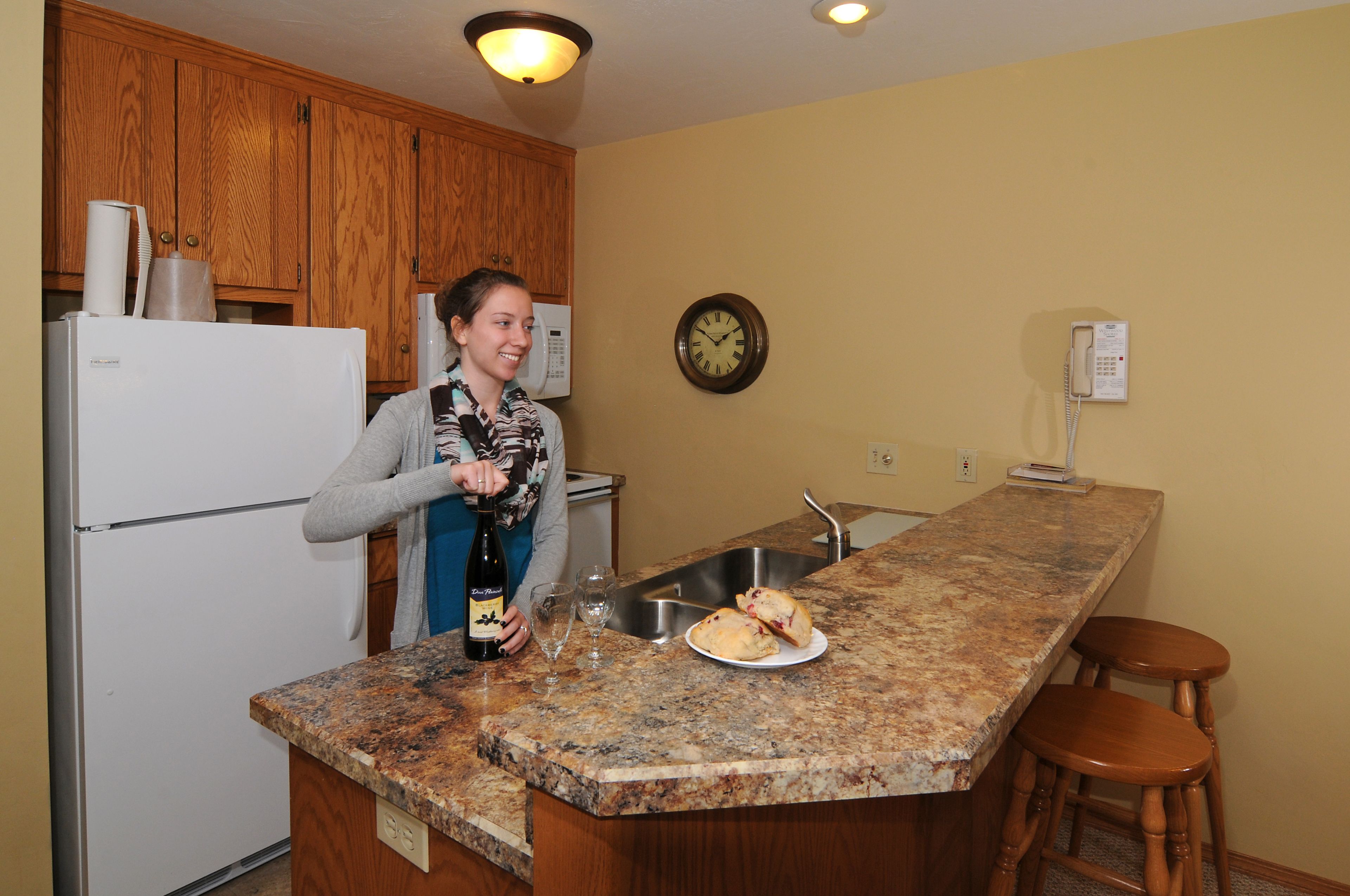 A kitchen with wooden cabinets, a granite countertop, a sink, and a clock on the wall.