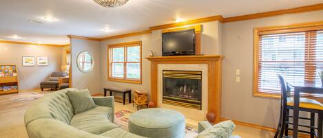 A living room with a large L-shaped sectional sofa, a fireplace, a television on a mantel, and a dining area with a table and chairs.