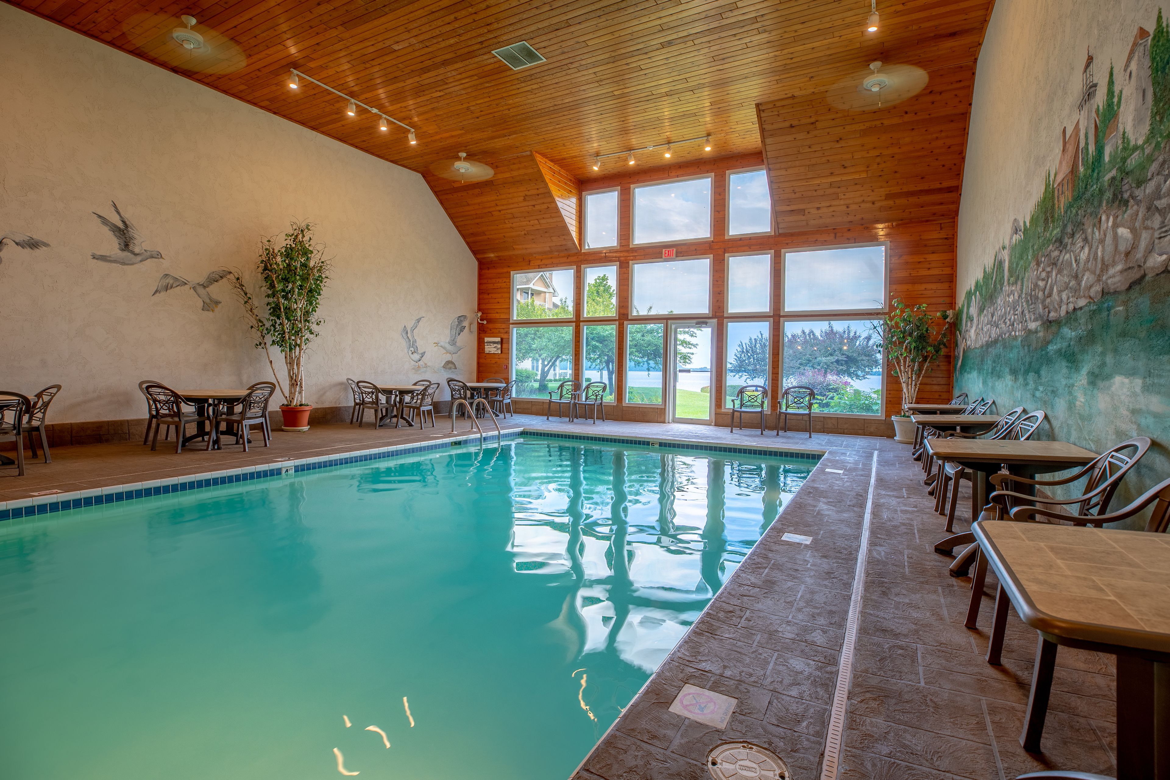 An indoor swimming pool with wooden ceiling and walls, surrounded by tables and chairs.