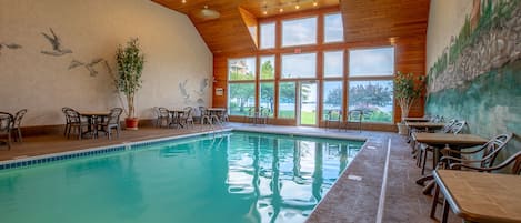 An indoor swimming pool with wooden ceiling and walls, surrounded by tables and chairs.
