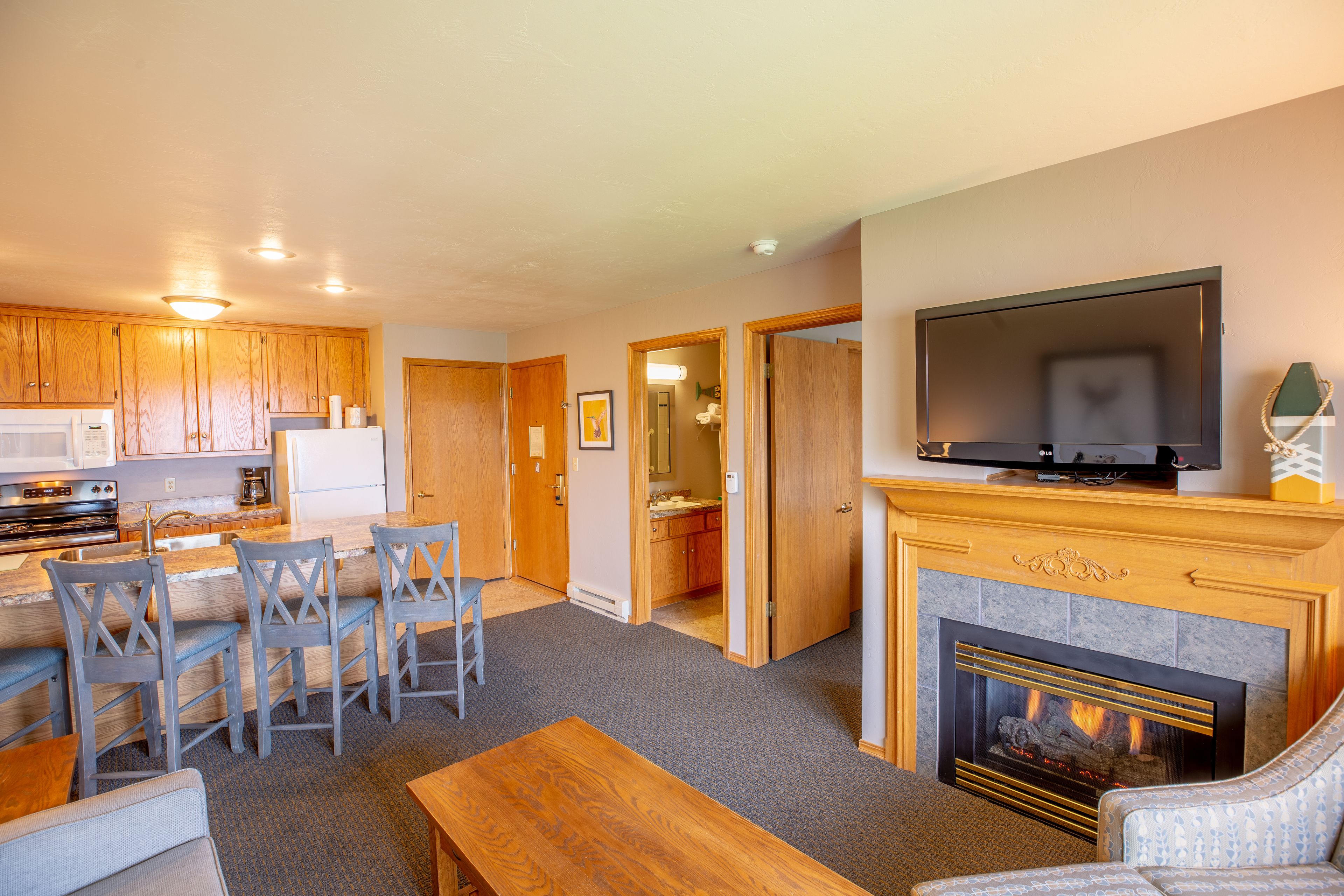 A modern living room with a fireplace, a television, and a kitchen area with wooden cabinets and a dining set.
