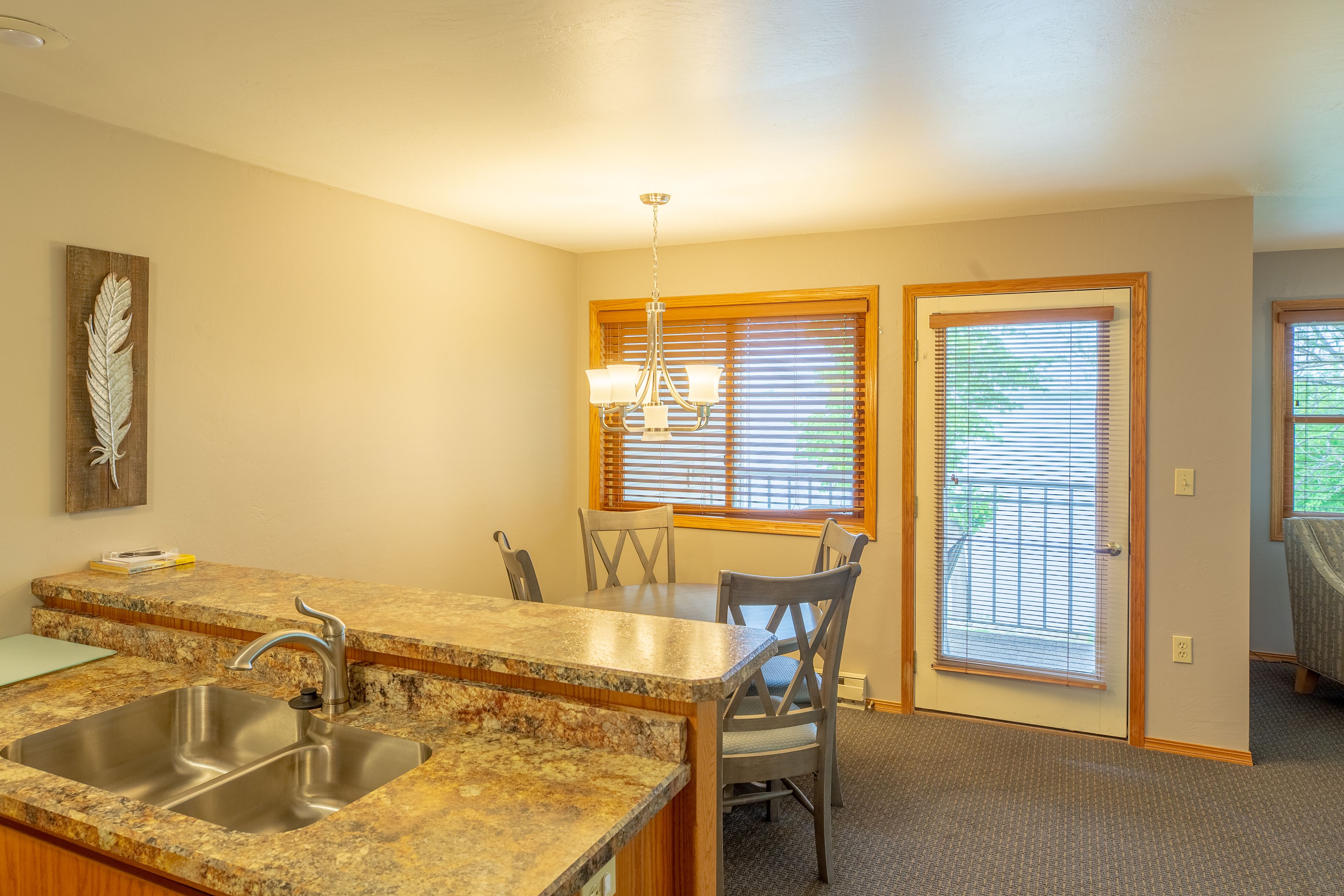 A kitchen with granite countertops, a double sink, and a dining area with a table and chairs.