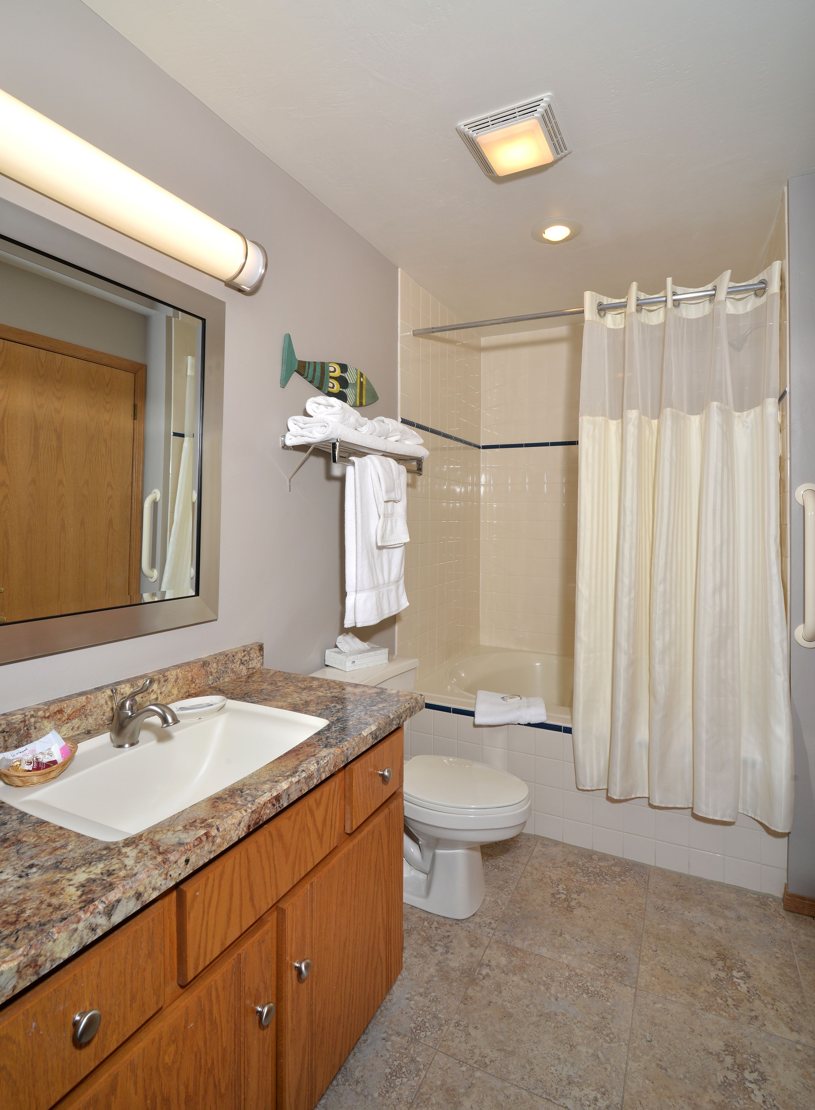 Een badkamer met een marmeren aanrechtblad, een wastafel, een toilet, een douche met gordijn en een spiegel.