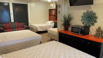 A hotel room with two beds, a TV, a microwave, a potted plant, and a statue.