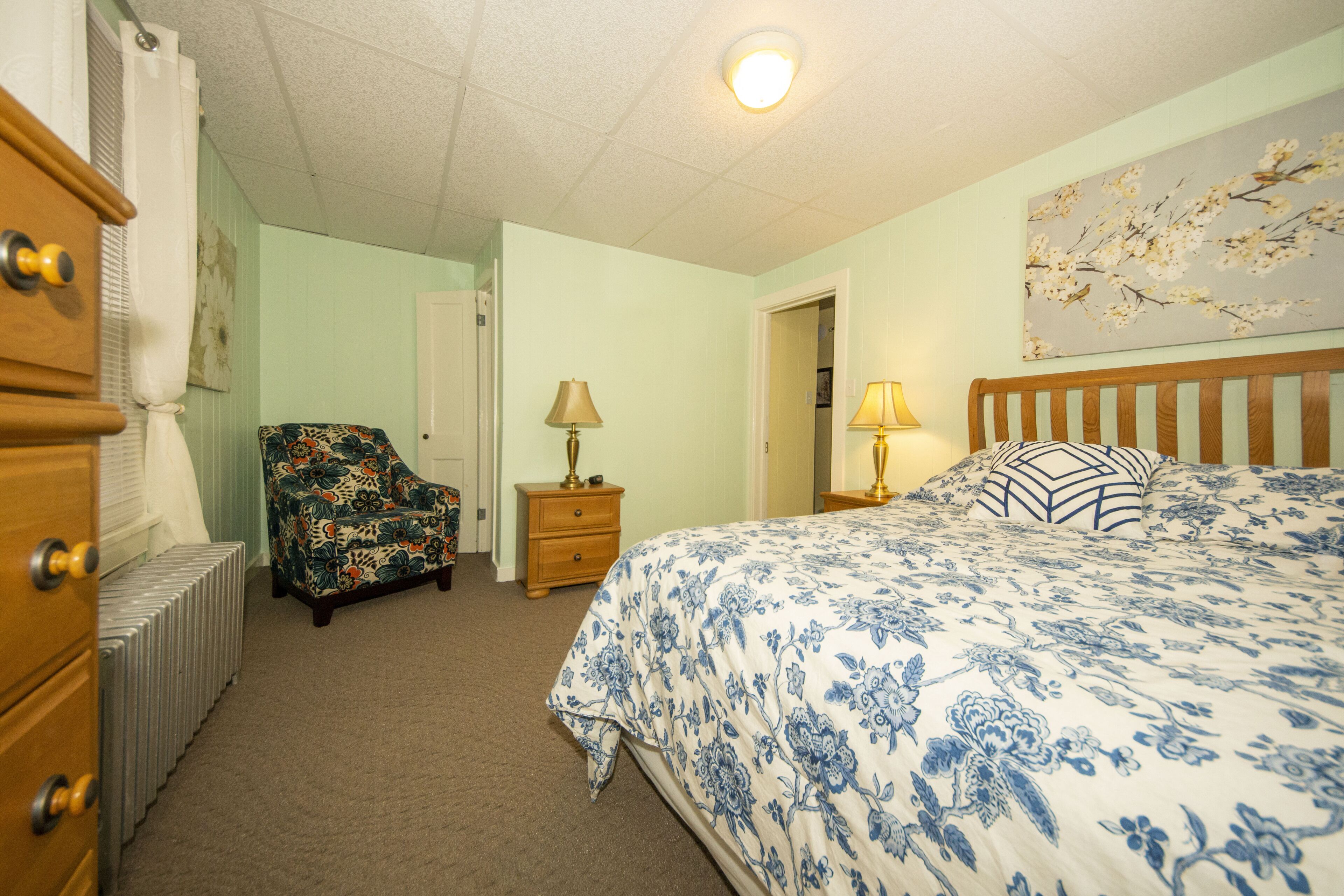 A bedroom with a bed, dresser, chair, and a radiator.