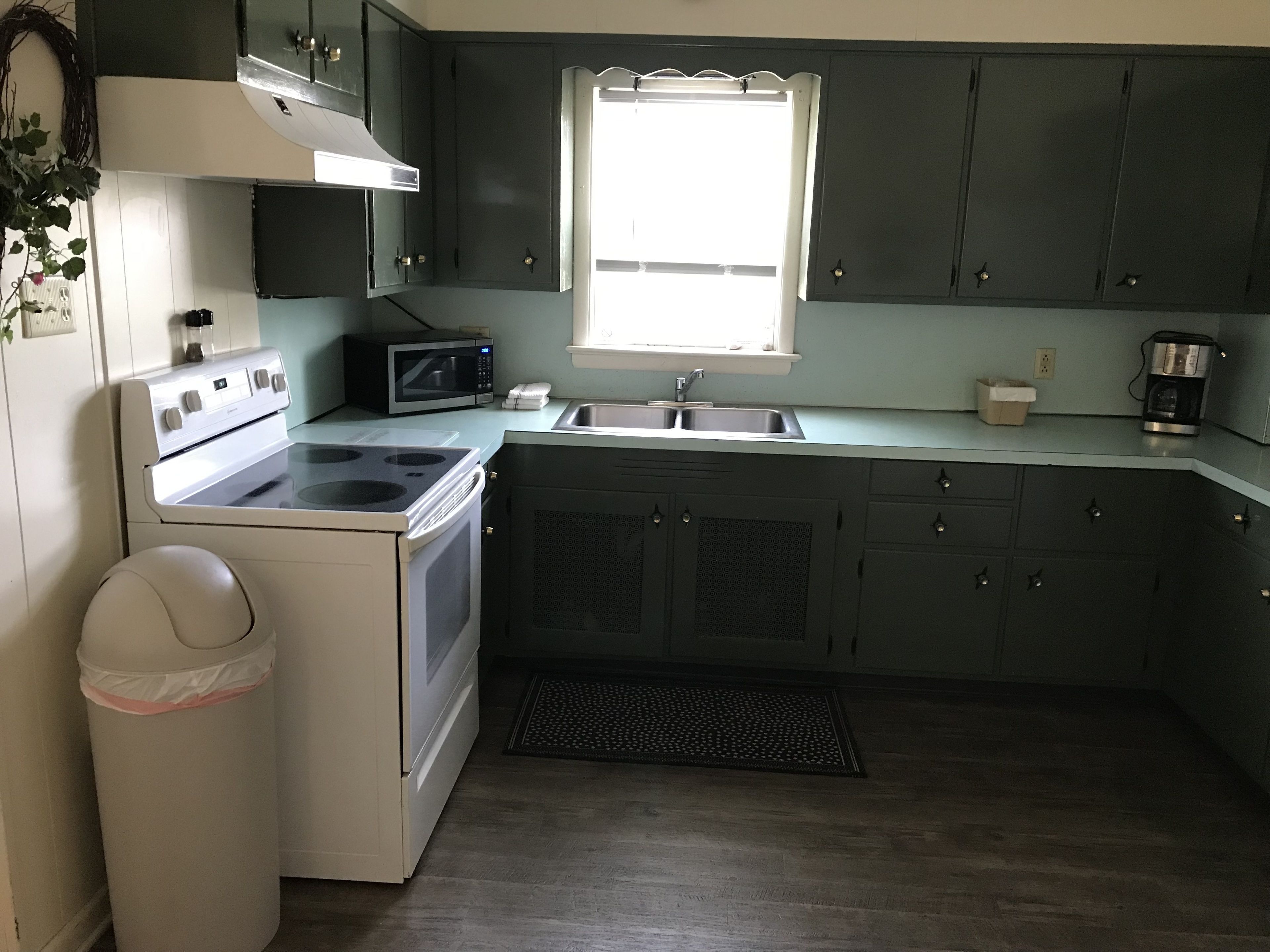 Una cocina con armarios oscuros, una estufa blanca, un microondas, un lavaplatos y una ventana.