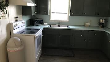 Una cocina con armarios oscuros, una estufa blanca, un microondas, un lavaplatos y una ventana.