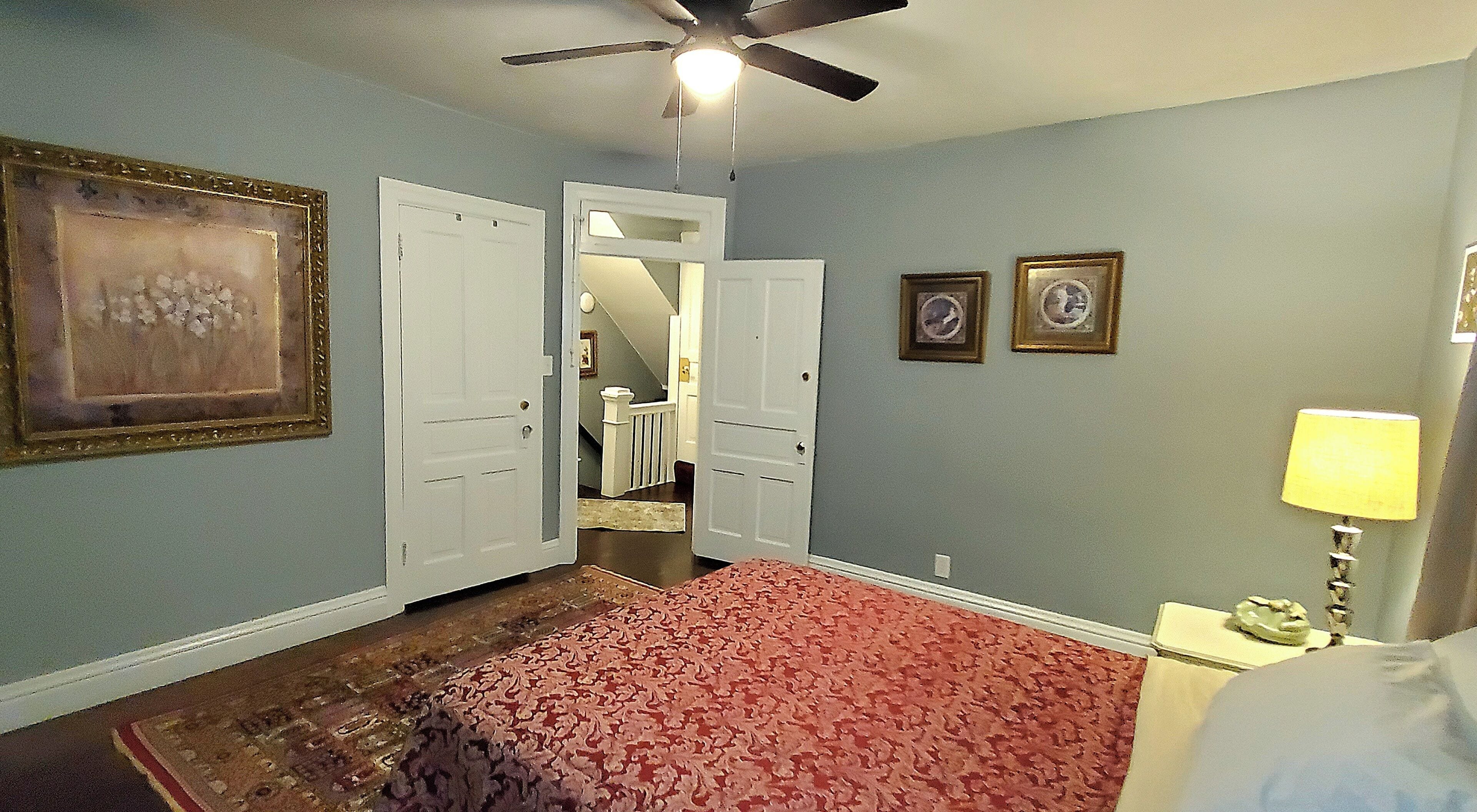 A room with a ceiling fan, a red patterned carpet, and a bed.
