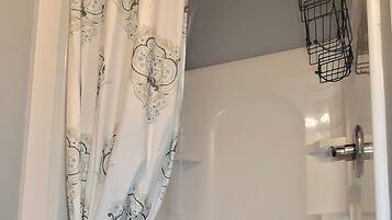 Um chuveiro com cortina branca estampada com padrão paisley, um cesto de metal para acessórios de banho e uma banheira branca.