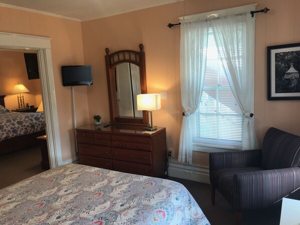 A bedroom with a bed, dresser, chair, and a window with curtains.