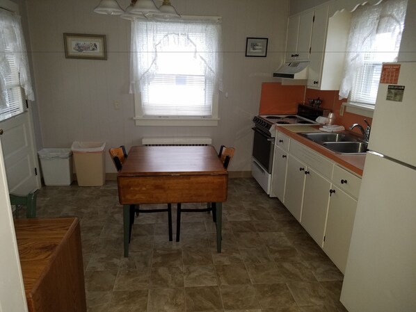 A compact kitchen with a dining table, a stove, a sink, and cabinets. - Simmons Motel (Hershey)