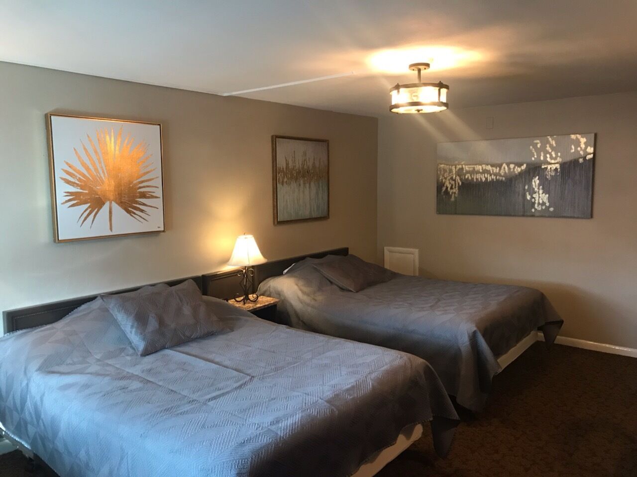 Habitación de hotel con dos camas, una mesita de noche con lámpara y tres obras de arte colgadas en la pared.