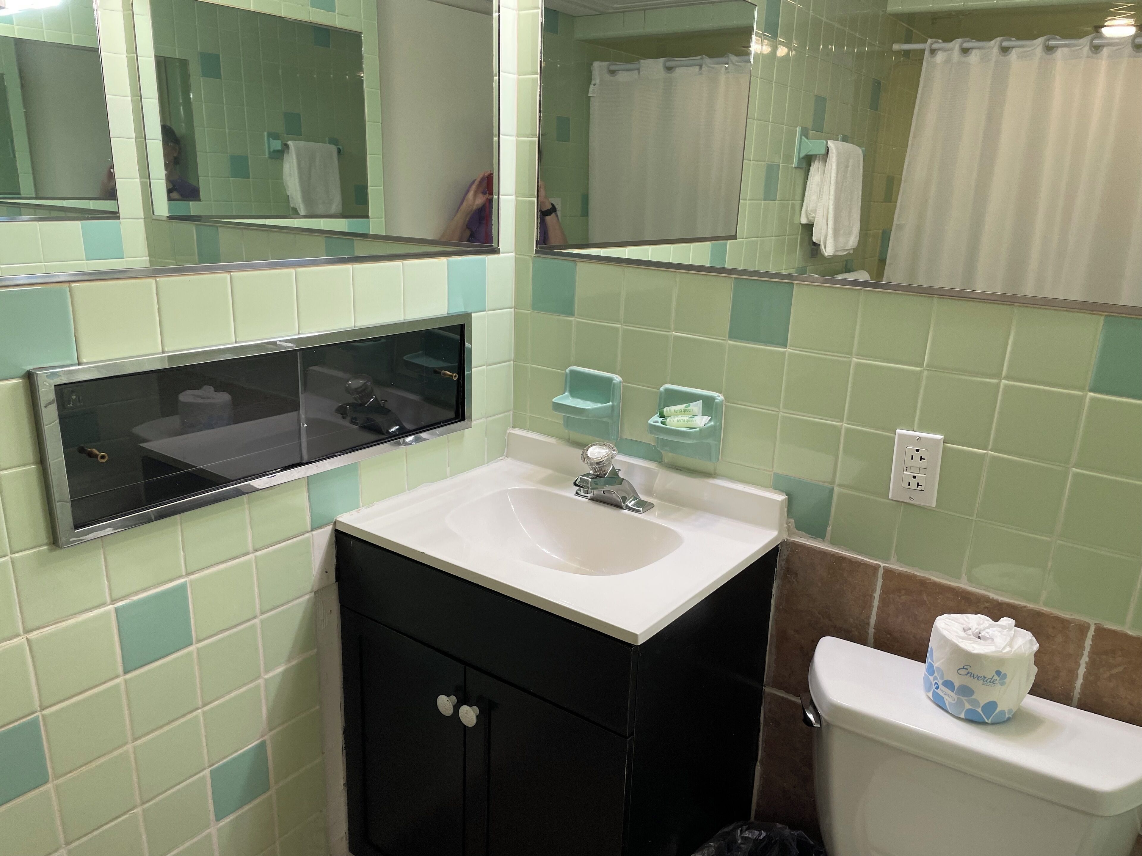 A bathroom with a white sink, black cabinet, and a toilet. There is a mirror above the sink and a shower curtain in the background.