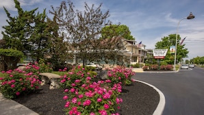 A street view with a Simmons Motel sign, a stone bench, and pink flowers. - Simmons Motel (Hershey)