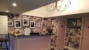 A reception area with a checkered floor, a reception desk with framed photos, a chandelier, and a floral wallpaper. - Simmons Motel (Hershey)